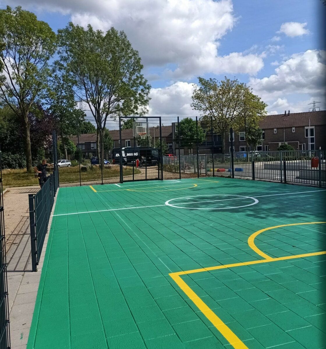 Waarom wij voor veel pannakooien nog steeds gewone betontegels adviseren 4 Voetbalkooi met basketbal en een Granuplast groene rolcoating als speelvloer.